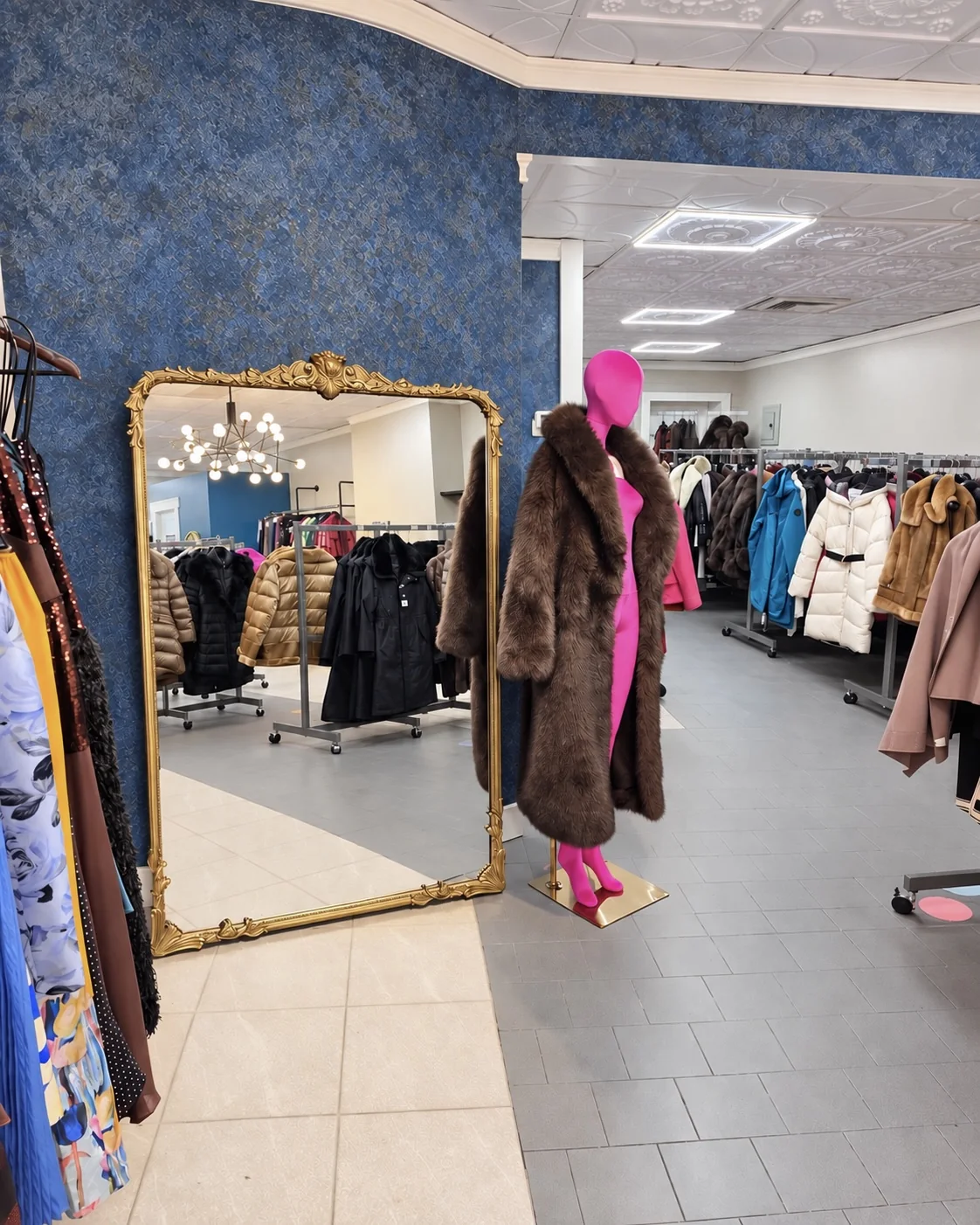 A gold-framed full-length mirror and fuchsia mannequin against a deep blue wall
